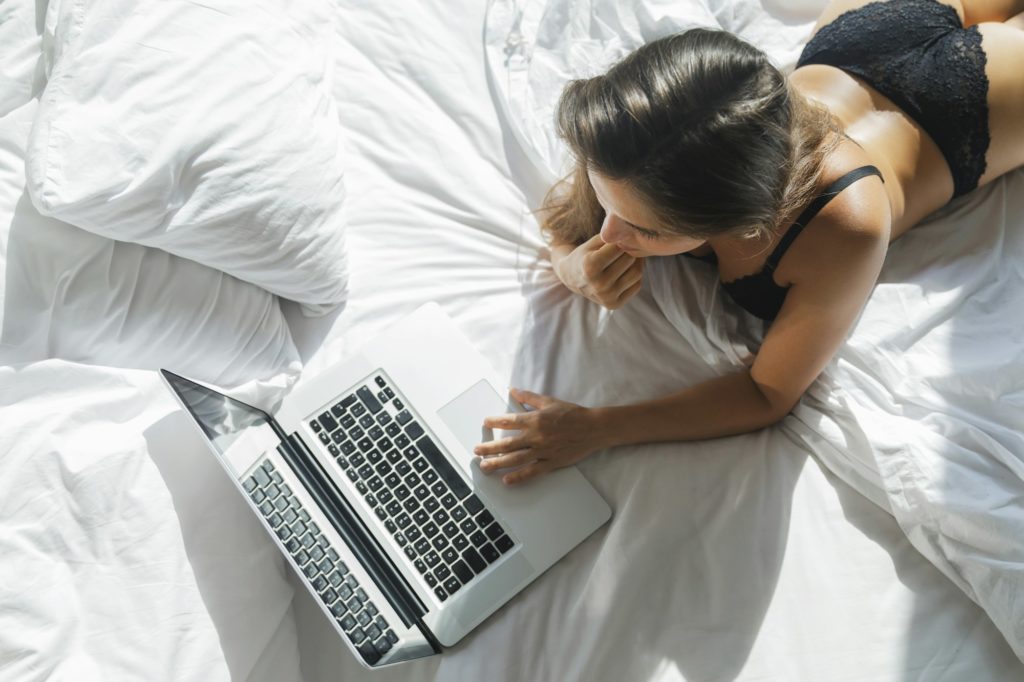 Sexy woman in black lingerie lying on the bed and using laptop
