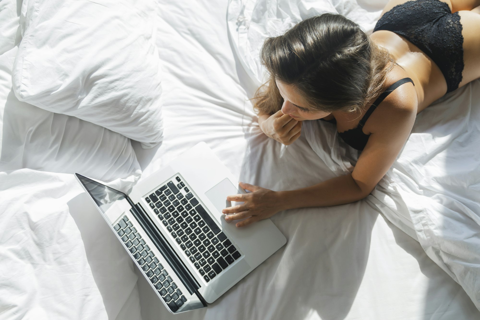 Sexy woman in black lingerie lying on the bed and using laptop